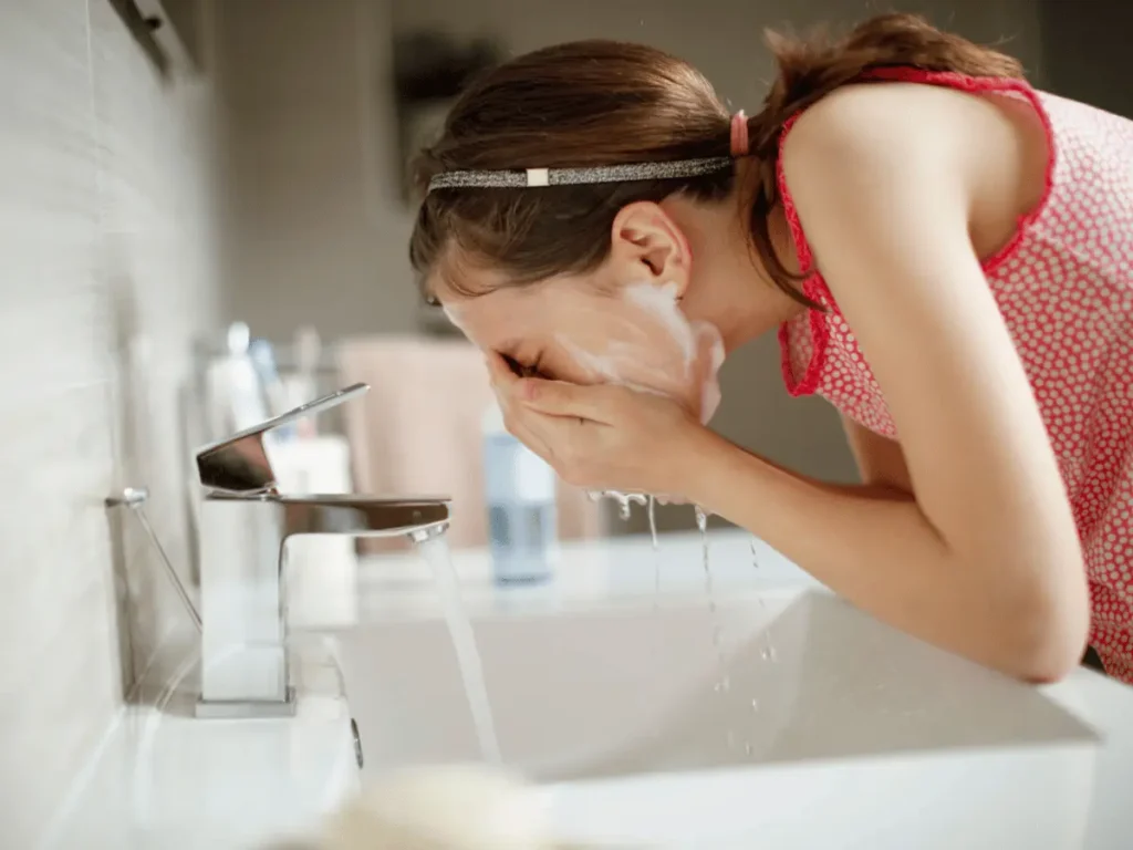 Woman washing her face at the sink, a key step in morning skincare routine
