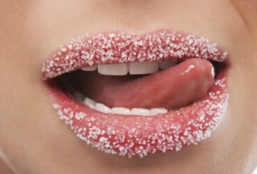 Applying sugar lip scrub to dry, chapped lips for exfoliation.