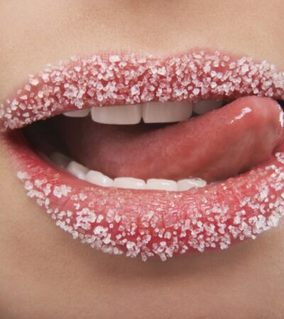 Applying sugar lip scrub to dry, chapped lips for exfoliation.