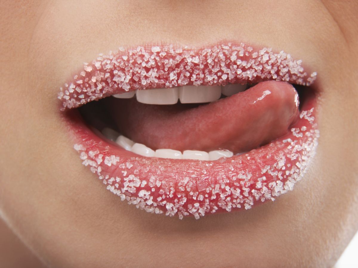 Applying sugar lip scrub to dry, chapped lips for exfoliation.