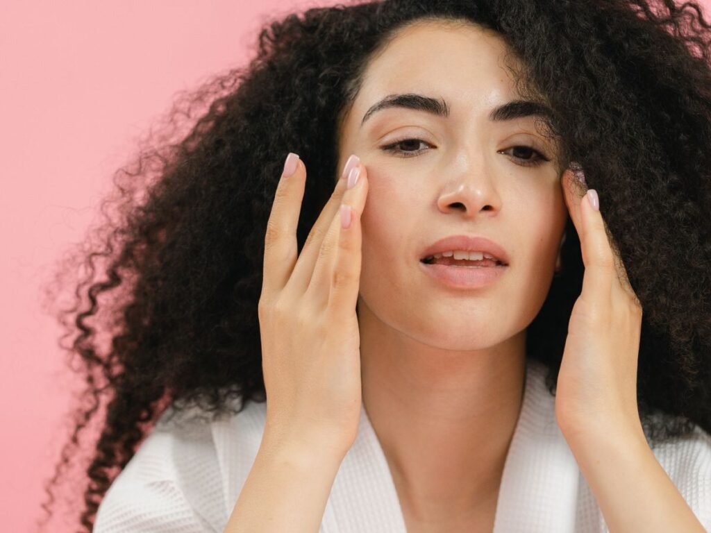 Woman with curly hair touching both cheeks, showing a simple skincare routine for oily skin