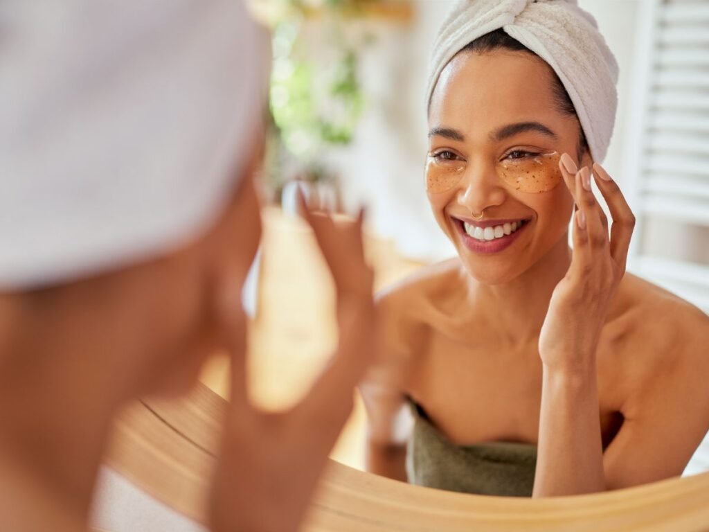 Smiling woman with a towel on her head and under-eye patches, following the best skincare tips for dark skin tone