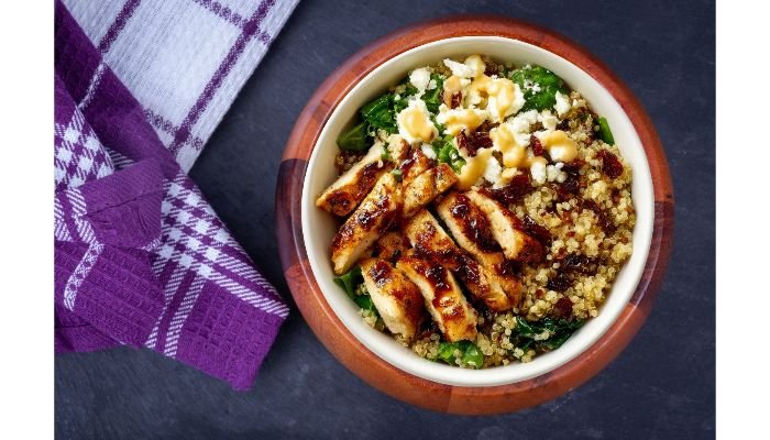 Healthy chicken and quinoa bowl with glazed sliced chicken, spinach, sun-dried tomatoes and crumbled cheese