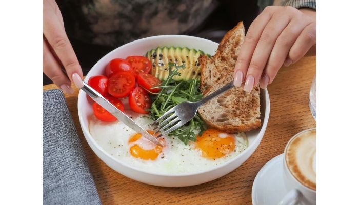 Healthy breakfast bowl with two sunny-side-up eggs, sliced avocado, cherry tomatoes, arugula and whole grain toast