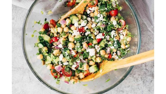 Mediterranean chickpea salad with cucumber, tomato, red onion, parsley and feta in a glass bowl
