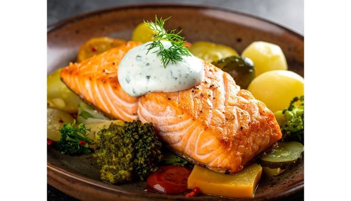 Pan-seared salmon fillet topped with dill yogurt sauce, served with baby potatoes and broccoli