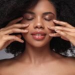 Woman with glowing skin gently touching her face with both hands, the kind of results people look for in Alloy skincare reviews